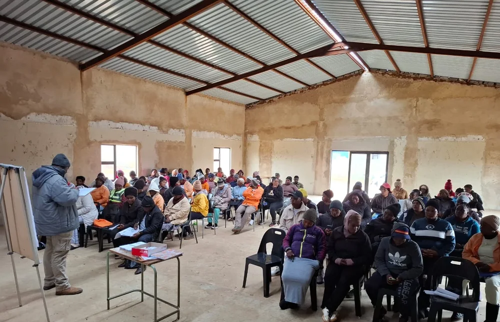 A facilitator leading a business skills training session for community participants in a rural hall